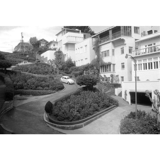 This black-and-white photograph from the 1950s captures the iconic, winding Lombard Street in San Francisco, USA. In the...