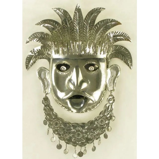 Stamped and cut polished metal tribal mask. Foliate headdress, pierced and plated lower lip with pierced ears joining...
