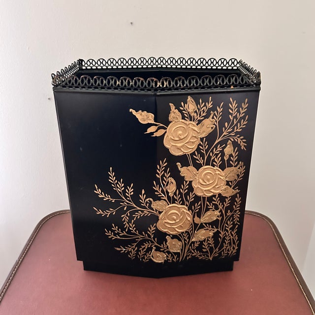 A vintage Wolff Products Co. metal toleware wastebasket with a black ground, textured gold floral decoration, and open...