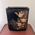 A vintage Wolff Products Co. metal toleware wastebasket with a black ground, textured gold floral decoration, and open...