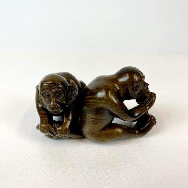Hand carved in hard wood. There two monkeys are sitting side by side, one eating a piece of fruit. The artists name is...