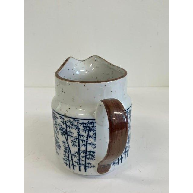 Vintage blue and white porcelain pitcher featuring a delicate bamboo motif and hand-applied brown rim detail. Perfect as a...