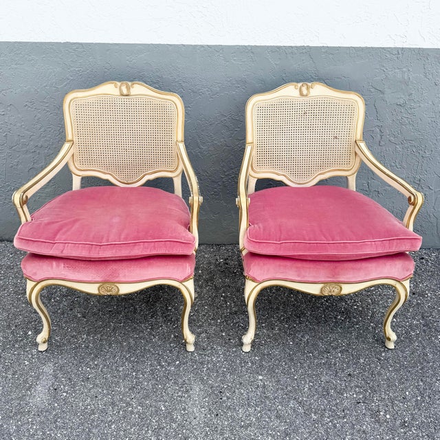 A charming pair of vintage French Provincial armchairs featuring cream-painted wood frames accented with gold detailing....