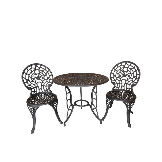 A sculptural mid-century garden bistro set in heavy cast iron, featuring an intricate hummingbird and vine motif...
