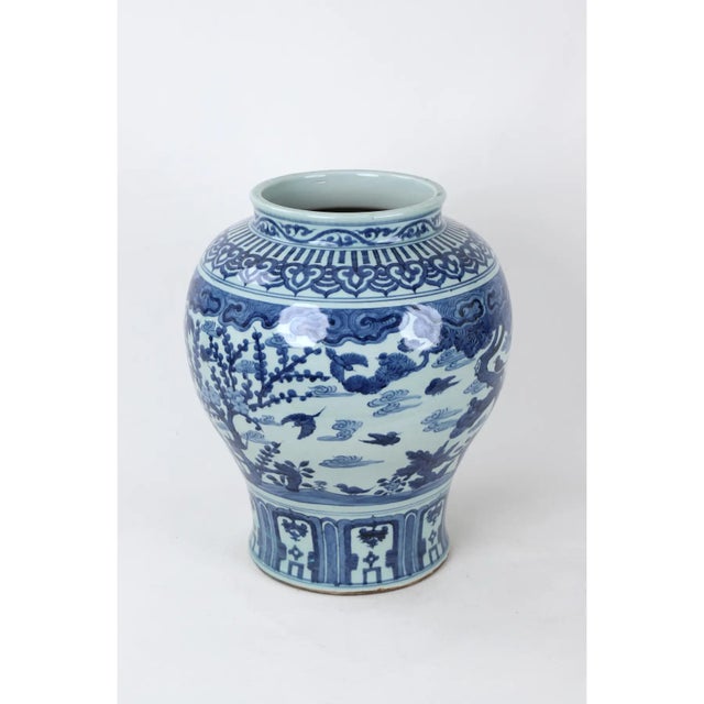 This blue and white temple vase features birds flying in a sky with clouds, framed by trees and a collar of medallions and...