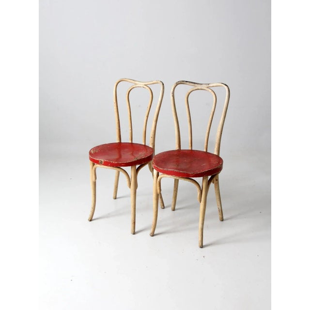 A pair of antique bentwood café chairs featuring classic, timeless lines. Each chair retains its original cream and red...