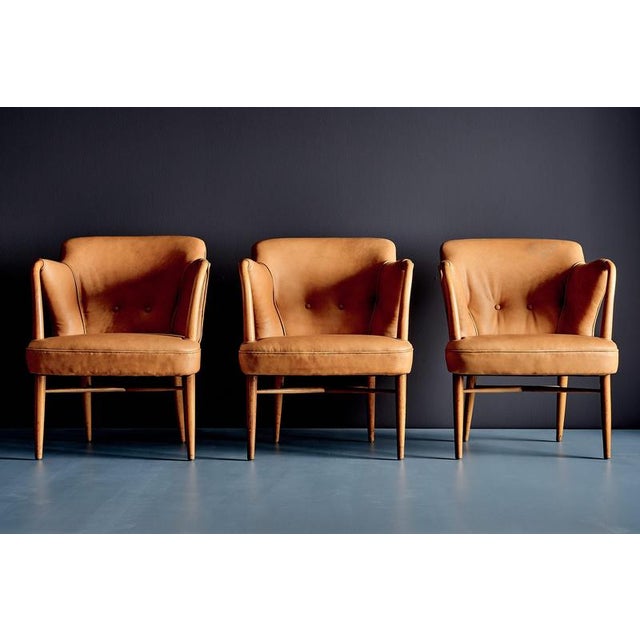 Set of three elegant 1950s lounge chairs with sculptural curved armrests, tapered wooden legs and newly upholstered cognac...