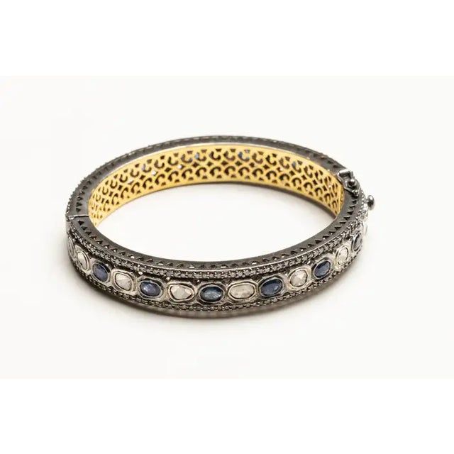A lovely bangle bracelet with alternating rosecut diamonds and oval, faceted blue sapphires all bordered on both sides...