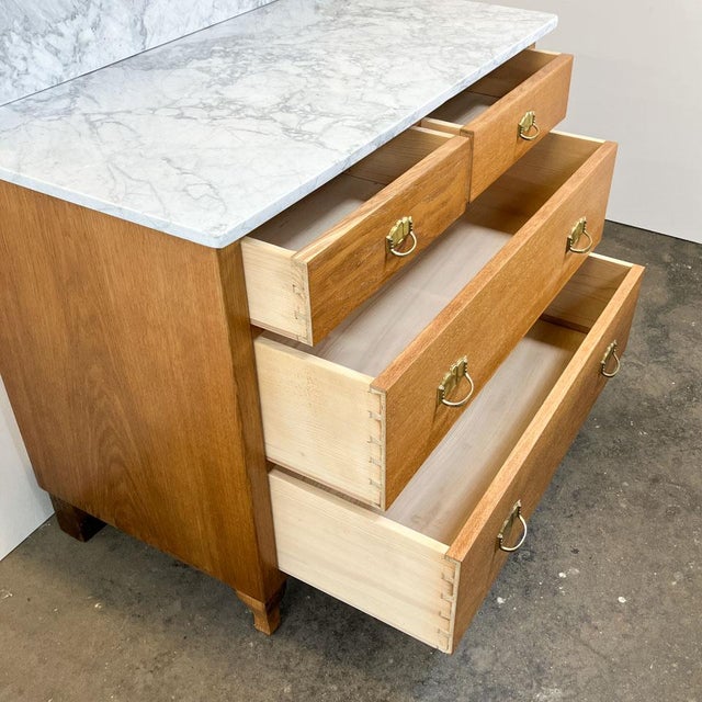 A beautiful Art Nouveau chest of drawers (1912) in a warm oak tone, featuring a marble top and a beveled mirror. Above...