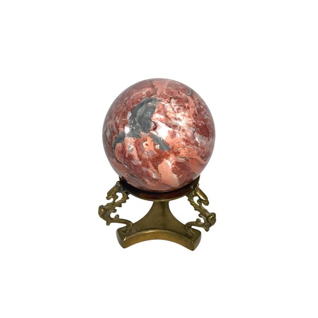A polished pink, red, and gray marble sphere on an ornate brass dragon stand, ideal for adding sophistication to your home...