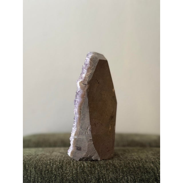 A natural amethyst geode specimen featuring a dense face of soft purple crystal points. The stone has been cut with a flat...