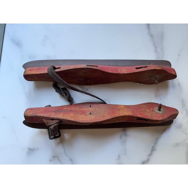 A pair of antique ice skates. Painted red wood and steel blades with leather straps. Nice for holiday decor.