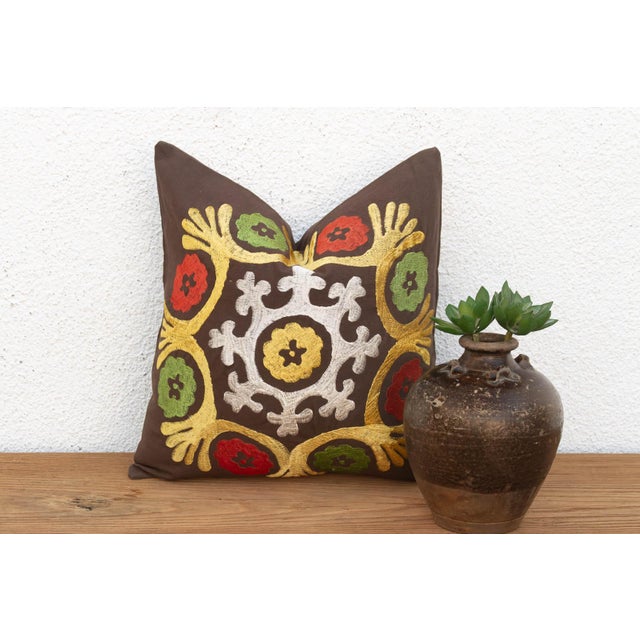 A stylized floral medallion anchors the center of this pillow — radiating mustard-gold tulip forms, pomegranate-red...
