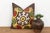 A stylized floral medallion anchors the center of this pillow — radiating mustard-gold tulip forms, pomegranate-red...
