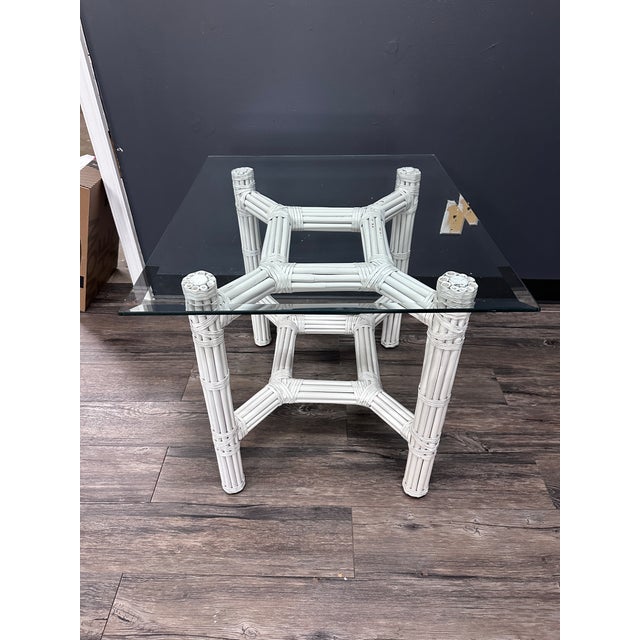 A chic white painted rattan table attributed to Ficks Reed, featuring a sculptural faux bamboo–style base and a clean,...