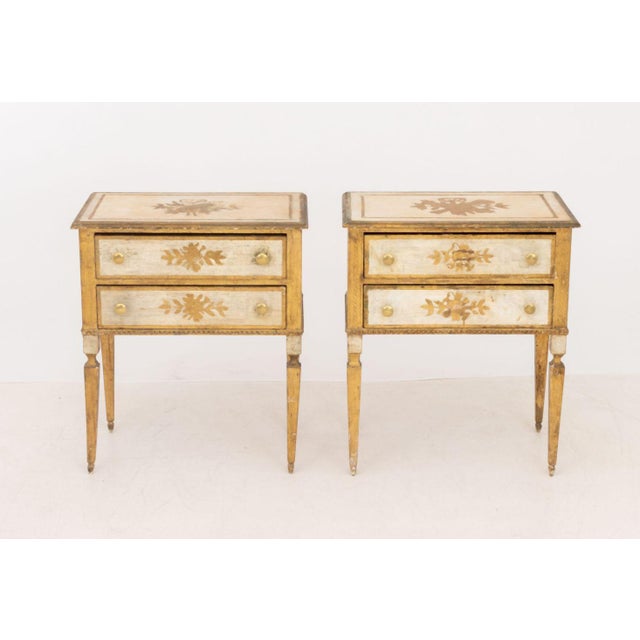 Pair of Louis XVI Style Distressed Side Tables, white painted with gilt decorated floral motif having two drawers on...