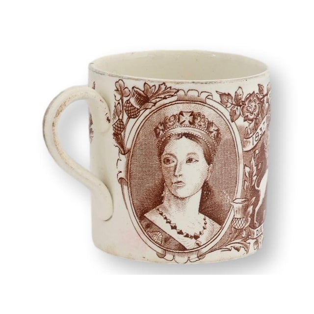 Commemorating Queen Victoria's Diamond Jubilee of 1897, this antique English commemorative mug features sepia transfer...