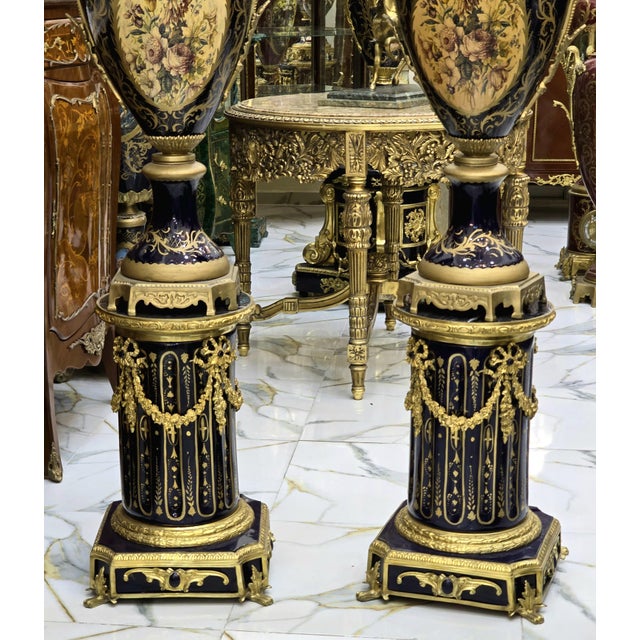An extraordinary pair of monumental Sevres-style porcelain vases, each perched on its own elegant pedestal. The hand-...