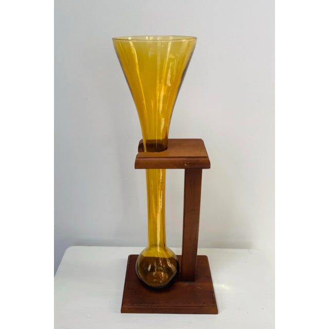 Elegant Mid-Century Modern vase featuring hand-blown amber glass in a sculptural teak-tone stand. Crafted in Italy’s...