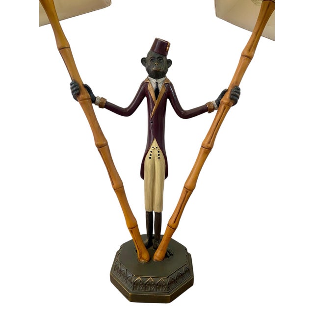 Hollywood Regency style table lamp featuring a monkey dressed as a bellhop and holding two bamboo "torches". Cast iron and...