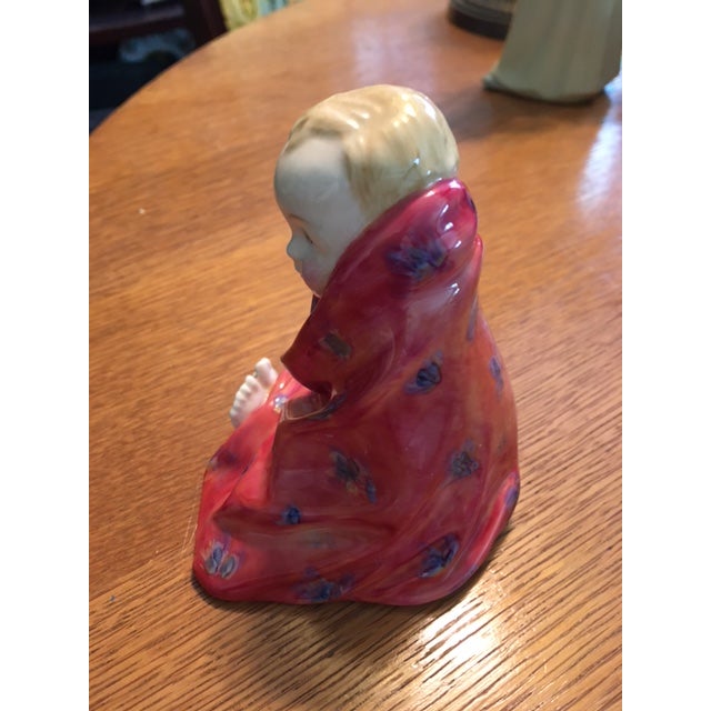 This Royal Doulton figurine is a little blond haired boy wrapped in a red blanket. He is called This Little Pig. The mark...