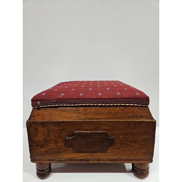 A unique square Victorian style footstool with burgundy upholstered top. This piece has carved wooden appliques to each...