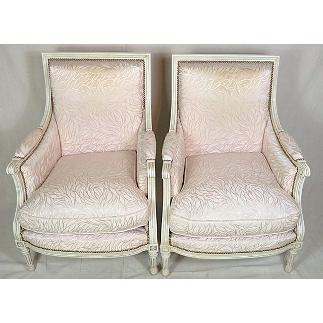 A pair of French bergeres in the style of Louis XVI and dating from the early 20th century. The chairs are stylish...