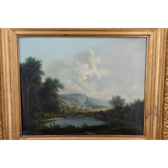 In the foreground, a lake surrounded by vegetation. On the left bank, several figures, some in a boat. In the background,...