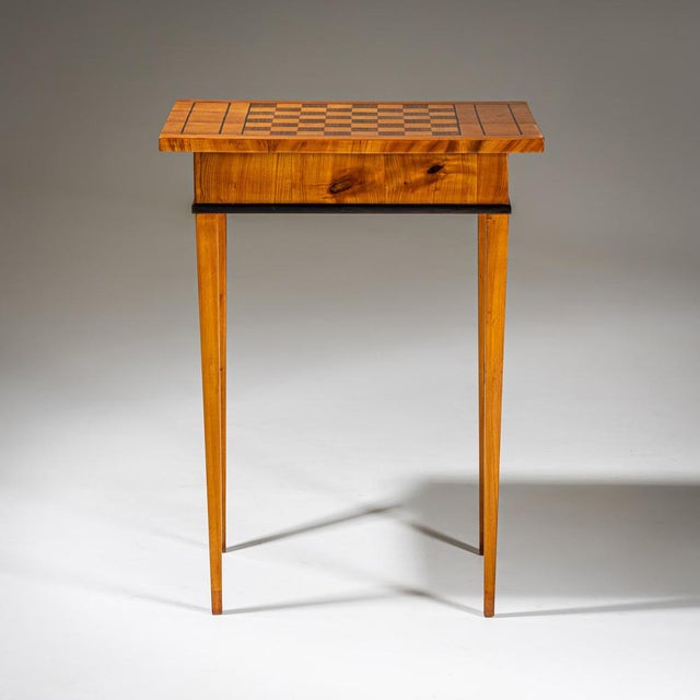 Side table in Biedermeier style on tall, tapered legs with a rectangular top featuring a chessboard design. The edges are...