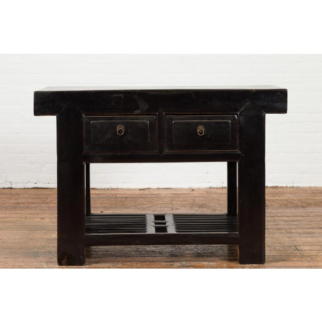 A Chinese black lacquered table from the early 20th century, with two drawers and open slatted shelf. Created in China...
