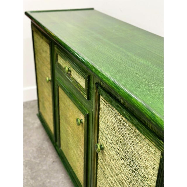 A striking vintage green lacquered sideboard featuring beautifully textured woven cane panels on each door and drawer. The...