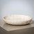 A large, heavy stone bowl crafted from beige travertine, featuring a minimalist design. Its gently sloping rim and flat...