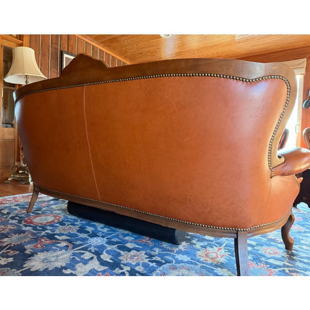 This striking antique-style leather sofa features a deeply tufted back, richly carved wooden frame, and elegant brass...