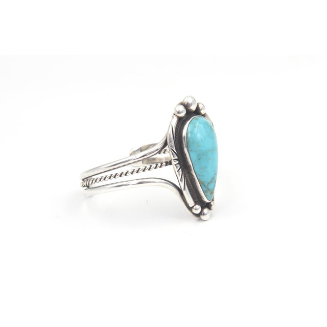 A striking Southwestern cuff bracelet featuring a vivid blue, teardrop-shaped turquoise cabochon in a darkened silver...
