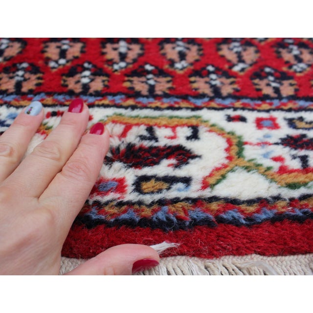 This vintage Indian wool rug presents a striking geometric composition set against a deep red field, framed by a richly...