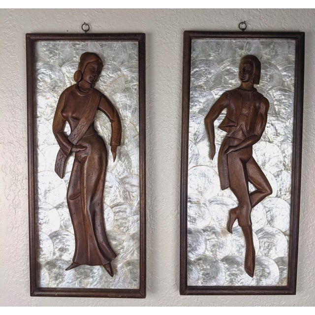 A striking and highly decorative pair of mid-century modern sculptural wall panels featuring deeply carved male and female...