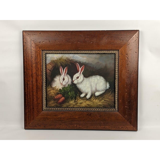 Charming vintage rabbit painting depicting a pair of softly rendered bunnies nestled among greenery and carrots, presented...