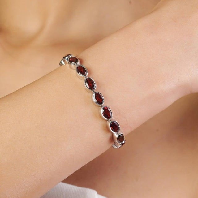 This stunning tennis bracelet is expertly crafted in 925 sterling silver and adorned with 22 natural oval-cut garnets,...