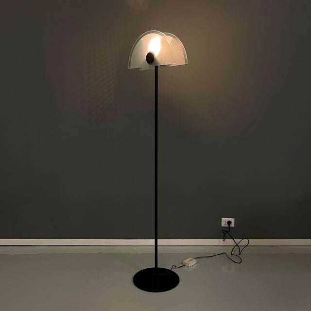 Floor lamp with half-moon lampshade in matt glass and black metal mesh. On the front of the lampshade there is a black...