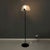 Floor lamp with half-moon lampshade in matt glass and black metal mesh. On the front of the lampshade there is a black...