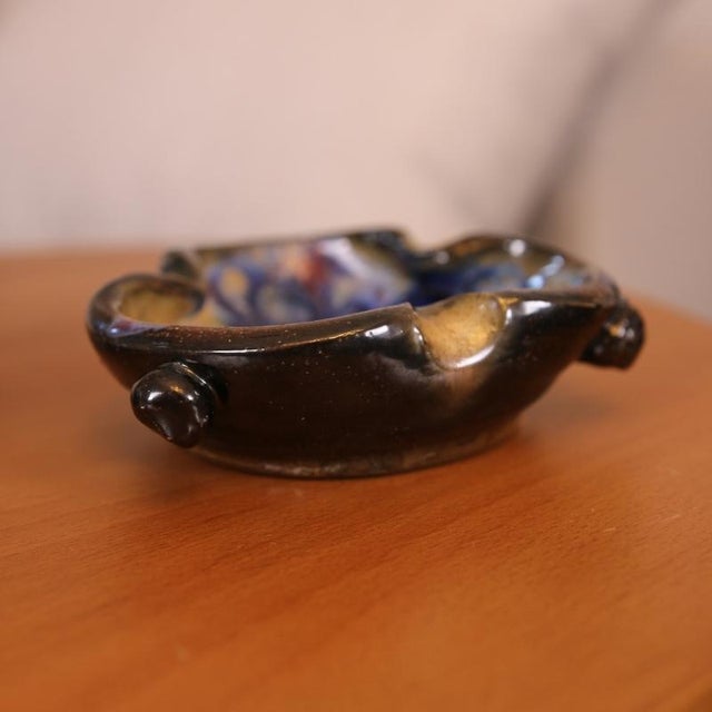 A stoneware trinket dish by roger guérin, dating from the first half of the 20th century. It features a brown base with...