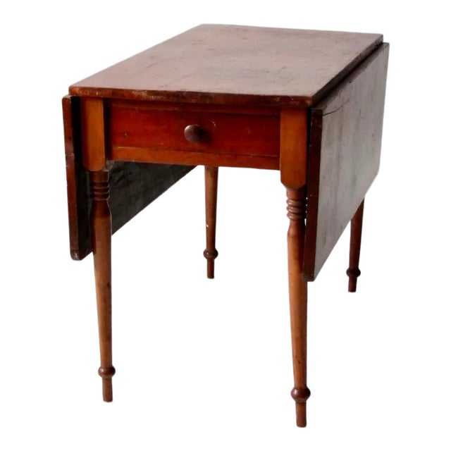 An antique wooden drop leaf table featuring a warm, richly toned finish and a versatile rectangular form. The table...