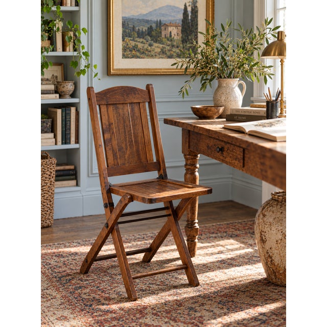An antique wooden folding chair featuring a paneled back, arched crest rail, and warm brown finish. The folding frame is...