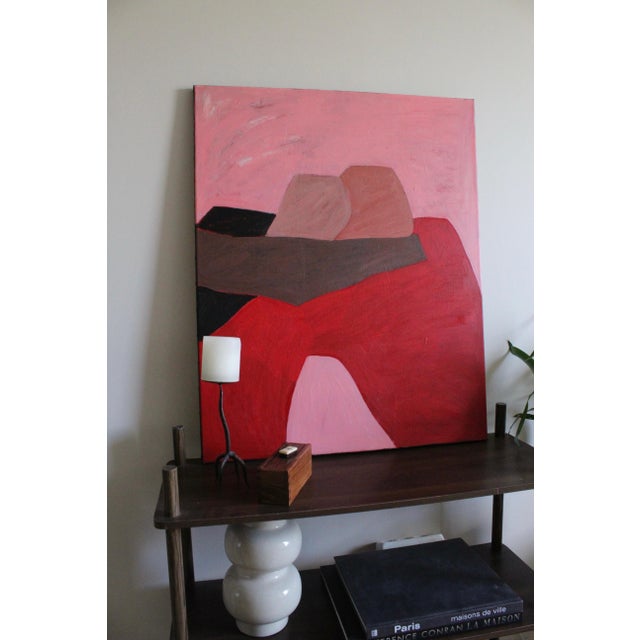 In this work, with its deep shades of red, powder pink, and earthy brown, two figures meet in a calm and silent embrace....
