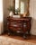 Elegant vintage Rococo-style chest featuring richly carved floral and scroll motifs throughout. Crafted in a warm dark...