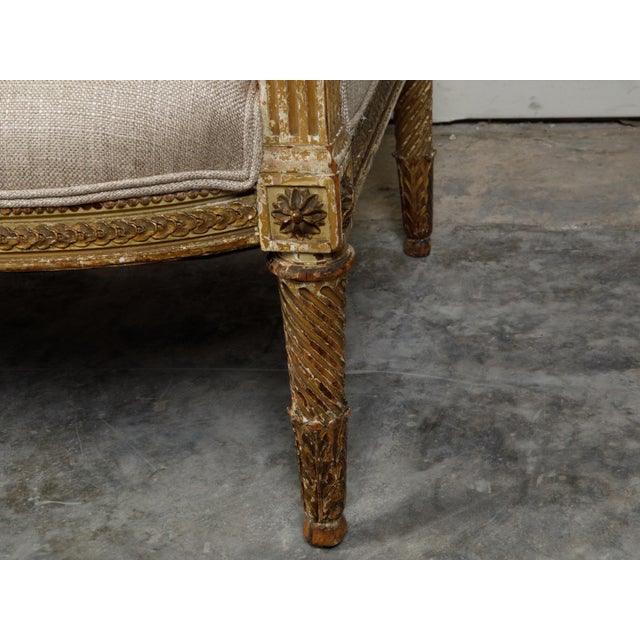 A French Louis XVI style giltwood wingback settee from the 19th century, with carved foliage motifs and distressed patina....
