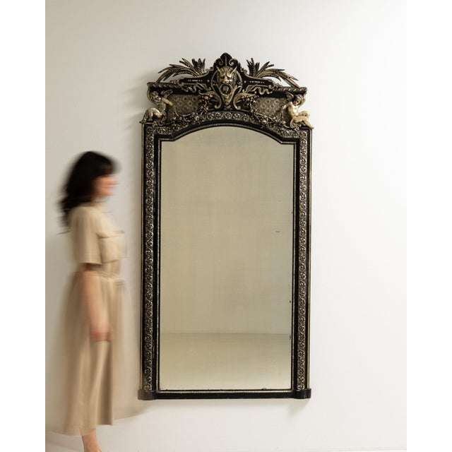 This mirror makes its impression through black frame with ornate gilt bronze crest, foliate motif. Originating in France...