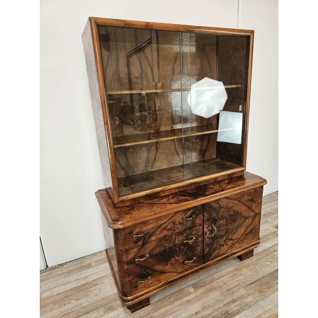 An elegant 1940s Art Deco double-body display cabinet, featuring a beautiful walnut burl veneer that highlights the...