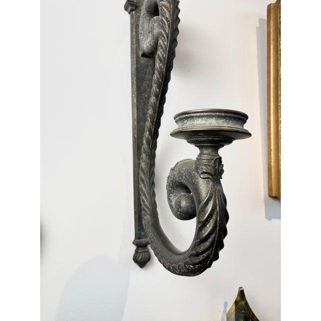 Dramatic vintage wall sconces in heavy cast metal (likely brass), with a long, curving tail that supports a single candle...