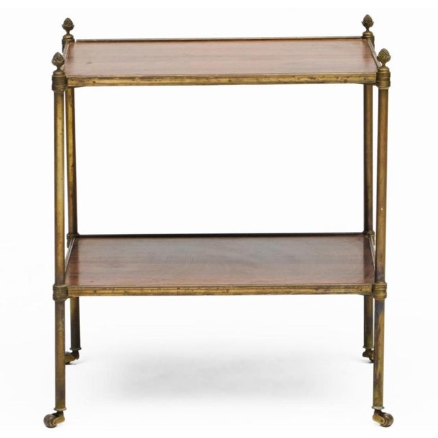 Classic chic 20th century two tier brass table in rosewood with lovely brass finials. Often mad by Jansen and popular by...